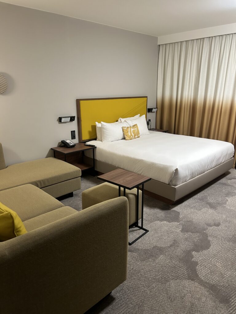 Spacious guest room with large bed and yellow sofa at Hyatt Place Paris Charles de Gaulle Airport 2