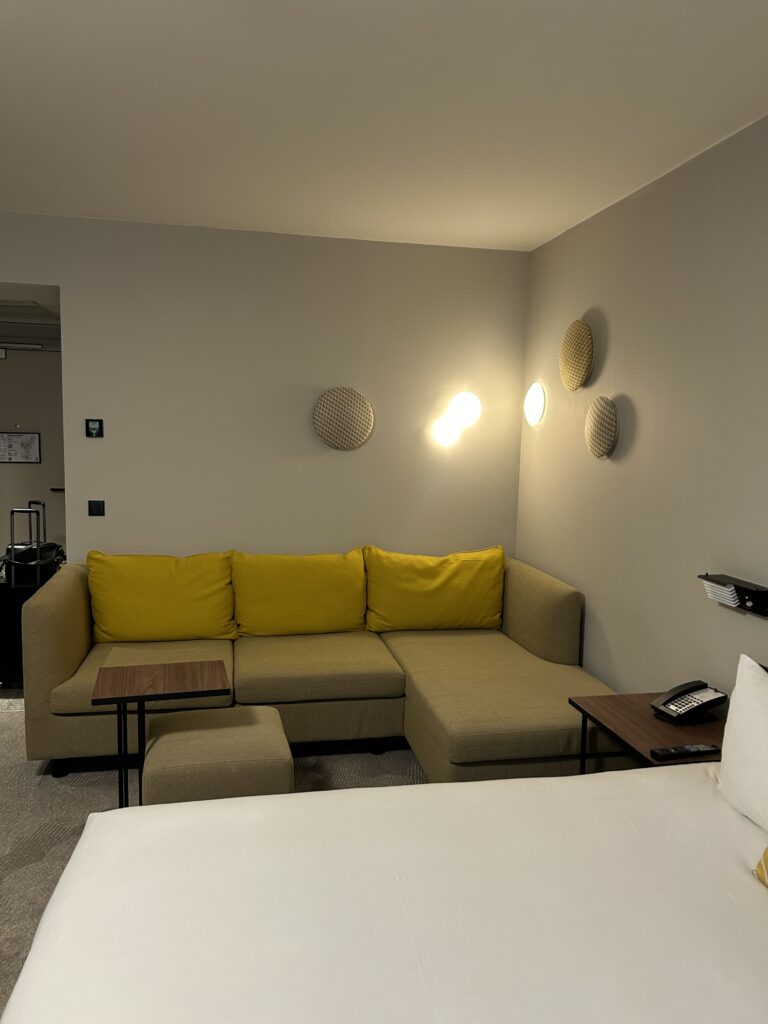 Comfortable seating area with deep yellow sofa in Hyatt Place Paris CDG hotel room